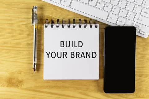 White notepad with text Build Your Brand lying on laptop on wooden table Stock Photos