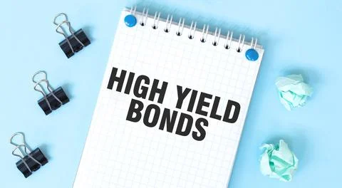 White notepad with text HIGH YELD BONDS and office tools on the blue backgrou Stock-Fotos