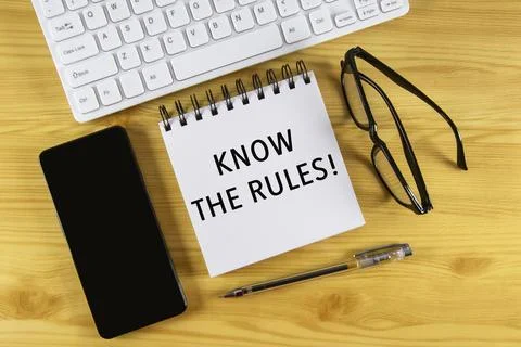 White notepad with text Know the rules lying on laptop on wooden table. Stock Photos