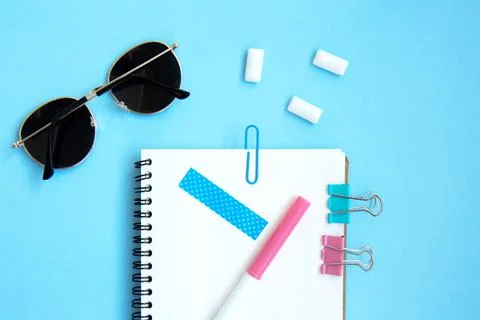White open notebook with blue elements, gum and sunglasses on a light blue ba 库存照片