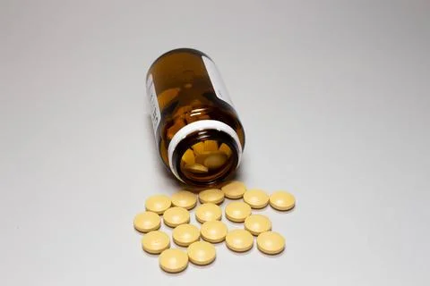 White open plastic jar with a bunch of white scattered pills on a light blue Stock Photos