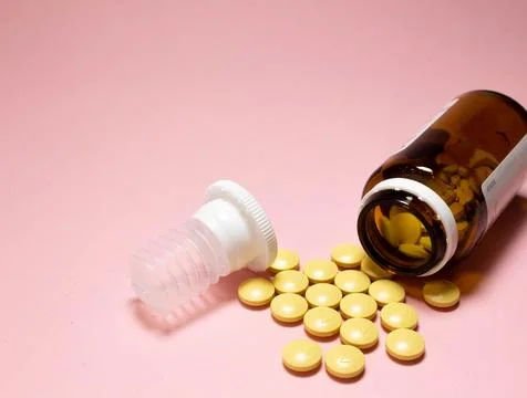 White open plastic jar with a bunch of white scattered pills on a light blue Stock Photos