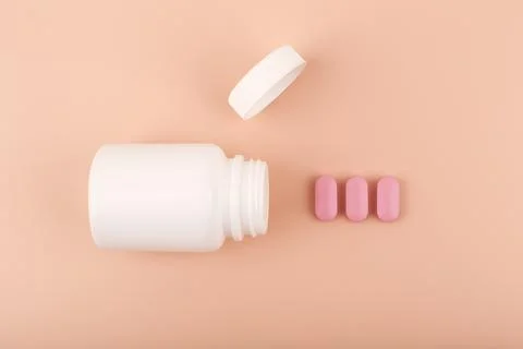 White opened medication bottle with pink spilled pills in a row against pastel Stock Photos