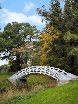 A white, openwork bridge over a stream in an autumn park against a blue sky Stock Photos