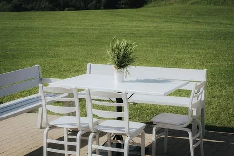 White outdoor dining table set with four chairs and a potted plant on a sun.. Stock Photos