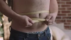 Obese man measuring waist with tape measure - SuperStock