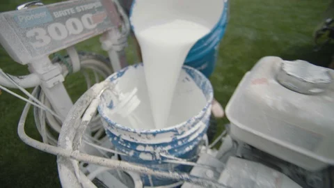 White paint being poured into spray paint bucket on equipment in football field Stock Footage 104768935