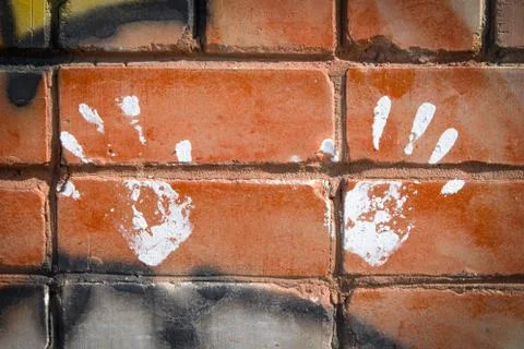 White paint prints of two hands on colourful graffity on a brick wall Stock Photos