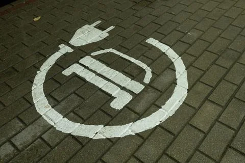 A white painted electrical plug and battery symbol on brick paving indicating. Stock Photos