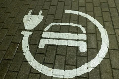 A white painted electrical plug and battery symbol on brick paving indicating. Foto stock
