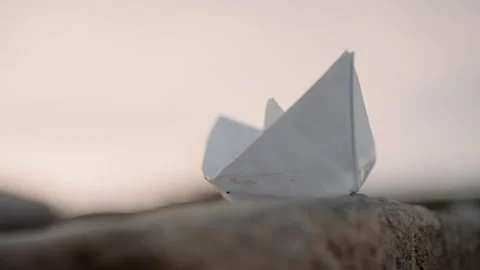 White Paper Boat Resting on Textured Stone with Soft Ambient Light showing Stock Footage 346733958