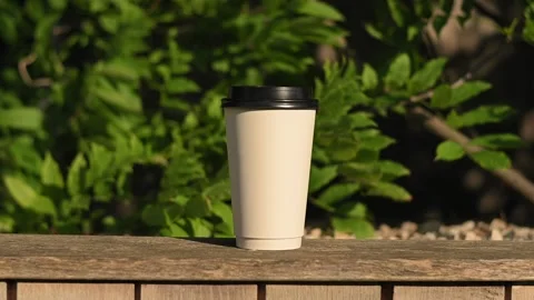 A white paper coffee tea cup with black plastic lid sits on wooden bench in the Stockbeeldmateriaal 199498316