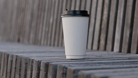 A white paper coffee tea cup with black plastic lid sits on wooden bench in the Stock Footage 199498788