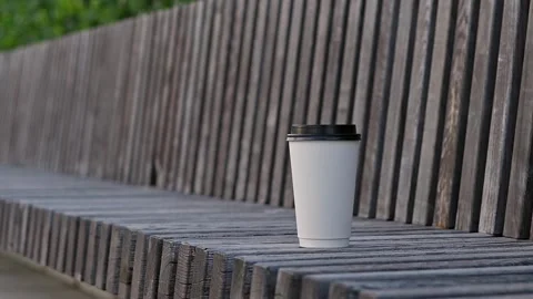 A white paper coffee tea cup with black plastic lid sits on wooden bench in the Stockbeeldmateriaal 199498860