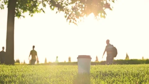 White paper coffee tea cup with black plastic lid stands on the green grass lawn Vídeo Stock 201382002