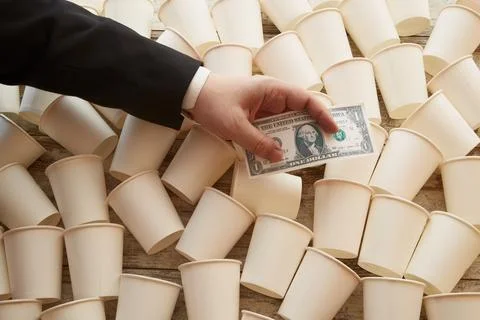 White paper cups scattered on the table and a businessmans hand holding a dol Stock Photos