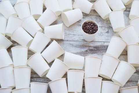 White paper cups scattered on the table and one with coffee beans among them Stock Photos