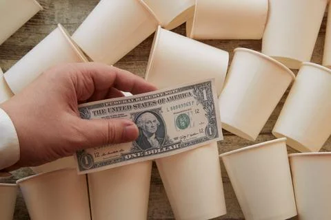 White paper cups scattered on the table and a businessmans hand holding a dol Stock Photos