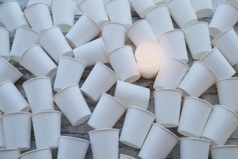 White paper cups scattered on the table and one is glowing with warm light. T Stock Photos