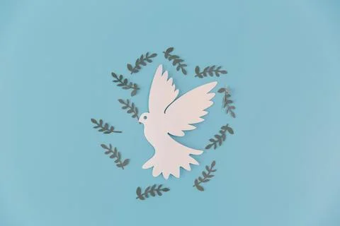 White paper-cut dove centered on a blue background, surrounded by olive lea.. Stock Photos