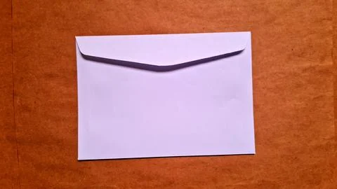 White paper envelope resting on a textured brown paper surface background Stock Photos