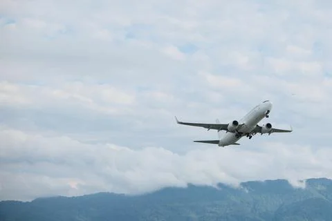 White passenger jet flying in the cloudy blue sky shortly after takeoff Stock Photos