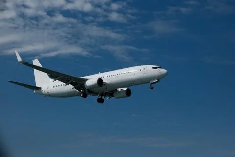 White passenger plane on final approach for landing against a blue sky Stock Photos
