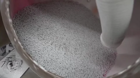 White pellets tumbling in a rotating coating pan while red colorant is dusted in Video stock 340901892