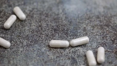White pills fall onto a dark surface.  Stock Footage 269905944