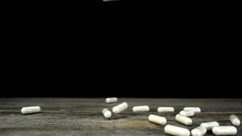 White pills fall in slow motion on a black Stock Footage 134309907