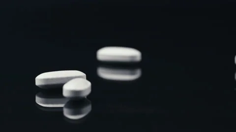 White pills falling on a black mirror surface Stock Footage 170602625