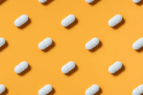 White pills lie in rows diagonal on orange background top view pattern. Stock Photos