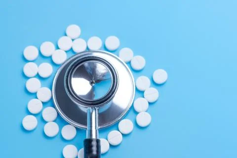 White pills or tablets and stethoscope on blue background Stock Photos
