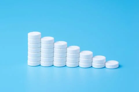 White pills or tablets stacked on each other in the form of steps on blue bac Stock Photos