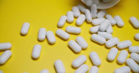 White Pills Spilling from Bottle on Bright Yellow Background Stock-Footage 307862729