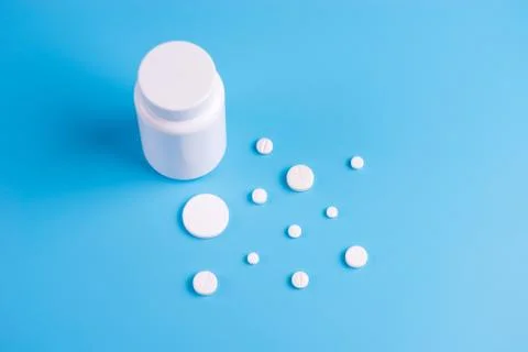 White pills, tablets and white bottle on blue background. Stock Photos