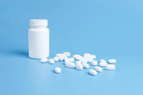 White pills, tablets and white bottle on blue background Stock Photos