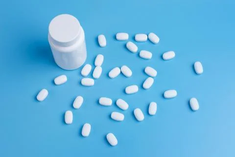 White pills, tablets and white bottle on blue background Stock Photos