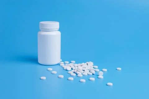 White pills, tablets and white bottle on blue background Stock Photos