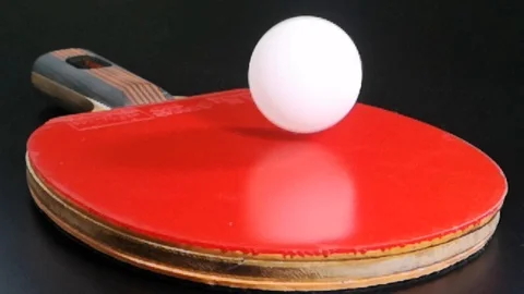 White ping pong balls bounce over red rubber racket.Slow motion Stock Footage 98356560