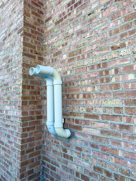 White pipe connected to brick wall at a building in sunlight during the day Stock Photos