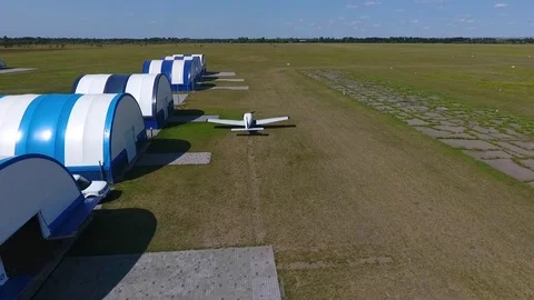 White plane takes off in the field passing by white blue hangars, air shooting Stock Footage 81549000