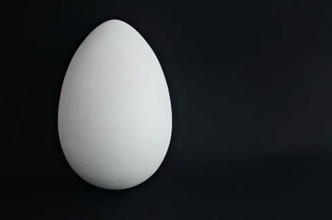White plaster egg on a black background. Abstract geometric shape. Copy space. Stock Photos