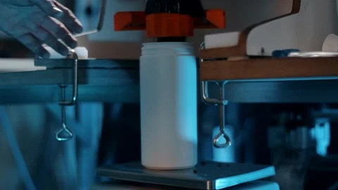 White Plastic Bottle Filling Under a Dosing Head, Blue Lit Workshop, Close Up Видео 341325784