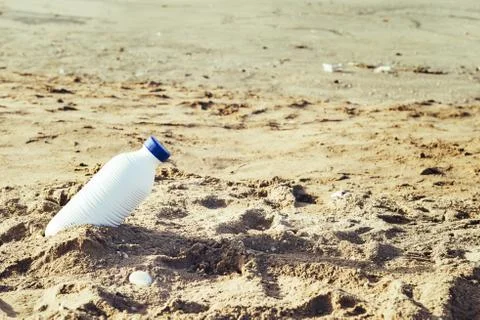 White plastic bottle lying on the beach sand Stock Photos