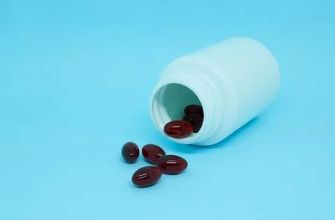 A white plastic bottle with scattered dark red capsules Stock Photos