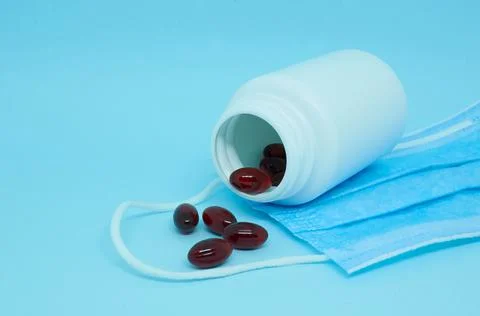A white plastic bottle with scattered dark red capsules and medical mask Stock Photos