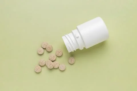 White plastic bottle with scattered tablets on pastel green background, minimal Fotos Stock