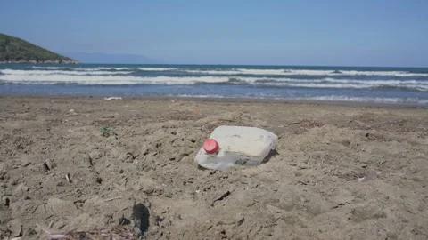 White plastic container lying on sand of sea beach against water waves. Video stock 146642566