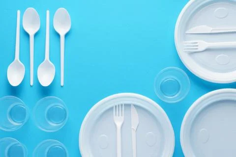 White plastic disposable tableware on blue background. Stock Photos